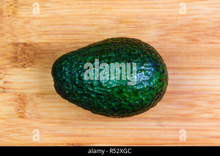 Ein ganzes hass Avocado auf einem Bambus Schneidebrett bereit, geschält und in Scheiben geschnitten, in einer Schale verwendet werden, einen Salat oder allein gegessen. Stockfoto
