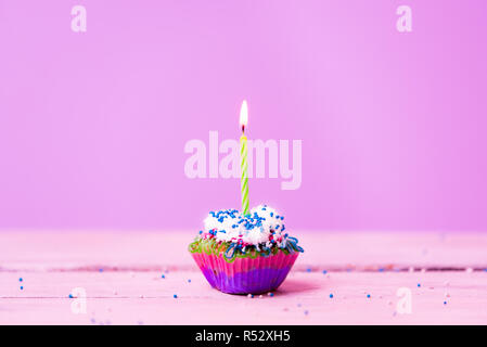 Pastellfarbenen Cupcake mit eine brennende Kerze in der Mitte von einem hellen violett-rosa Hintergrund Stockfoto