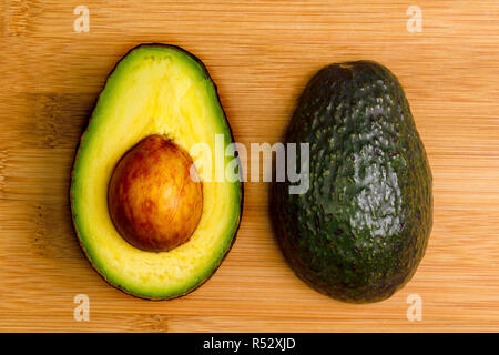 Zwei Hälften eines Avocado, 1 unten und 1 oben mit der Grube noch an Ort und Stelle, auf einem Bambus Schneidebrett. Stockfoto