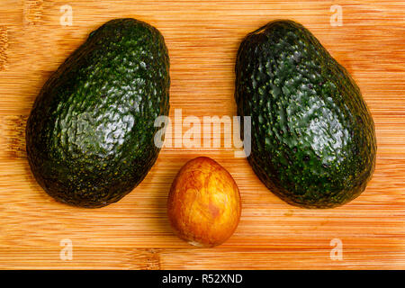 Zwei Hälften eines Avocado mit der Vorderseite nach unten auf eine Bambus Schneidebrett mit der Grube auf der Oberfläche zwischen ihnen. Stockfoto