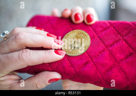 Virtuelles Geld goldene Bitcoin auf rosa Frauen Gewebe Geldbeutel. Finger mit roten Nägeln auf einer Münze Stockfoto