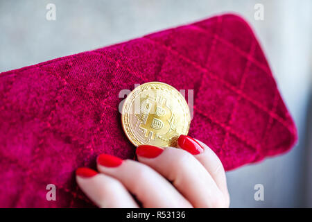 Virtuelles Geld goldene Bitcoin auf rosa Frauen Gewebe Geldbeutel. Finger mit roten Nägeln auf einer Münze Stockfoto