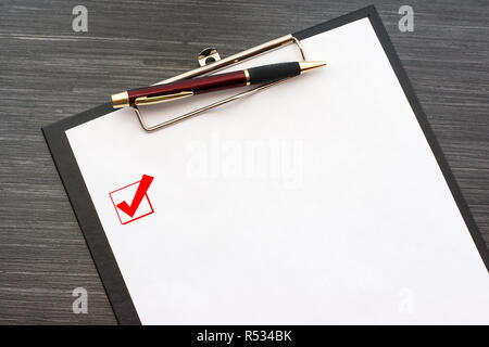 Schwarz, Klemmbrett mit weißen Blatt Papier und Metall pen auf dunklen Holztisch isoliert. Kontrollkästchen mit einem Haken auf der Seite. Ansicht von oben Büro Zubehör Stockfoto