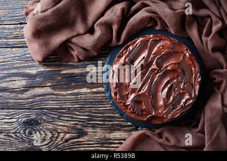 Schokoladentorte mit Marillenmarmelade und gekrönt mit Ganache auf einen schwarzen Stein Platte auf einem rustikalen Tabelle, Ansicht von oben, flach Stockfoto