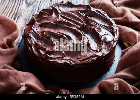 Nahaufnahme der hausgemachte Schokolade Fudge Kuchen gekrönt mit Ganache auf einem schwarzen Steinplatte mit braunen Tuch auf ein altes Holz- rustikalen Tisch, Blick fr Stockfoto