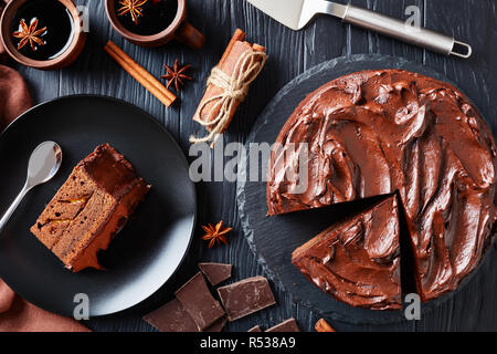 Nahaufnahme der hausgemachte Schokoladentorte mit Marillenmarmelade geschichtet und gekrönt mit Ganache auf eine schwarze Platte mit Glühwein aus Steingut serviert. Stockfoto