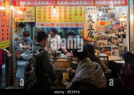 Die Menschen vor Ort kaufen Essen von einem Straßenhändler in Mong Kok. Hong Kong, Kowloon, Januar 2018 Stockfoto
