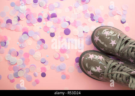 Die niedlichen Kind grün Schuhe mit Stern Print auf rosa Hintergrund mit bunten Konfetti ein Copyspace. Stockfoto