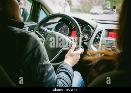 Man fährt ein Auto. Ein Kerl in einer Jacke sitzt hinter dem Steuer eines Autos fahren auf der Straße im Stau. Foto aus dem Sitz, durch Rücken des Fahrers Stockfoto