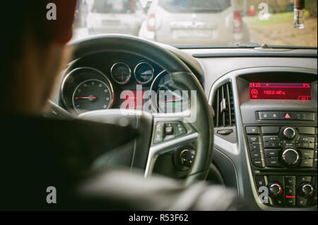 Man fährt ein Auto. Ein Kerl in einer Jacke sitzt hinter dem Steuer eines Autos fahren auf der Straße im Stau. Foto aus dem Sitz, durch Rücken des Fahrers Stockfoto