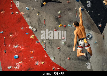 Junger Mann klettern in künstlichen Felsen, hängen an Sicherungsseilen Stockfoto