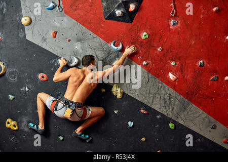 Junger Mann klettern in künstlichen Felsen, hängen an Sicherungsseilen Stockfoto