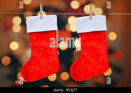 Weihnachten rote Socken mit einem Zapfen auf einem Seil eingehängt. Weihnachtsbeleuchtung und Bokeh im Hintergrund. Stockfoto