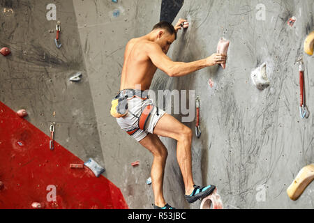 Männliche Kletterer das trainieren im Fitnessraum, Klettern bis auf künstliche Wand mit Felsbrocken. Stockfoto