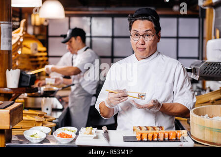 Schöner Mann holding Sushi mit Stäbchen Stockfoto