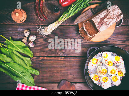 Gebratene Eier in eine Schwarze Pfanne, in der Nähe von Brot und frisches Gemüse Stockfoto