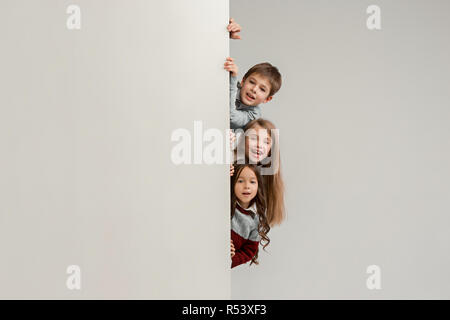 Banner mit einem überraschten Kinder peeking am Rand mit Copyspace. Das Porträt von niedlichen kleinen Kinder Jungen und Mädchen auf der Suche nach Studio Kamera gegen weiße Wand. Kids Fashion und glückliche Emotionen Konzept Stockfoto