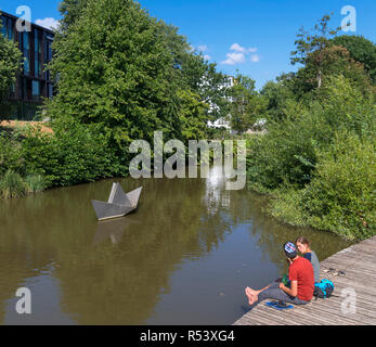 Paar auf die Waterfront mit Erik Heide Skulptur 'Papier' hinter dem Boot, Hans Christian Andersen Garten, Odense, Fünen, Dänemark sitzen Stockfoto