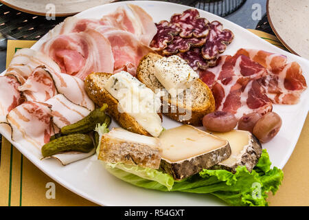 Auswahl an Aufschnitt und Käse mit Brot, Zwiebeln und Gurken, auf einem weißen Teller. Stockfoto