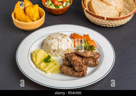 Türkisches Köfte auf einem Teller mit Reis, Kartoffeln und Gemüse, Brot, Pommes frites und Salat begleitet, auf schwarzem Hintergrund Stockfoto