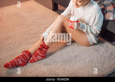 Schöne Frau in Weihnachten gemusterte Socken trinken Kakao Stockfoto