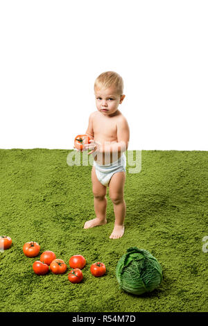 Cute Baby Boy holding Tomaten und Gemüse auf grünen Teppich Stockfoto