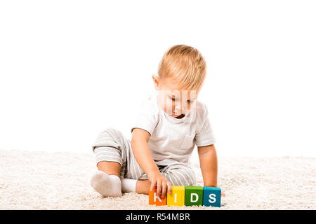 Niedliches Kleinkind Junge spielt farbige Würfel mit Buchstaben auf dem Teppich isoliert auf weißem Stockfoto