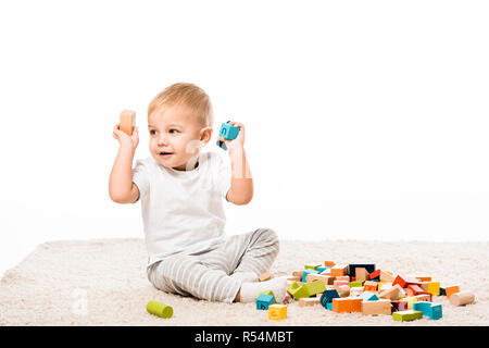 Adorable kleine Junge spielt mit Holzklötzen auf dem Teppich isoliert auf weißem Stockfoto