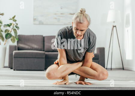 Erwachsene mann Üben Yoga zu Hause und tun Arm balance Übung mit gekreuzten Beinen, Maßstab der Körperhaltung, Tolasana, Utpluthi darstellen Stockfoto