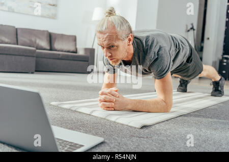 Sportliche erwachsene Mann tun Plank übung und Laptop Stockfoto