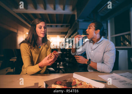 Geschäftskollegen essen Pizza, sitzen spät in der Nacht zusammen im Büro. Mann und Frau sitzen spät im Büro und essen nach Abschluss des Arbeitsauftrags Essen Stockfoto