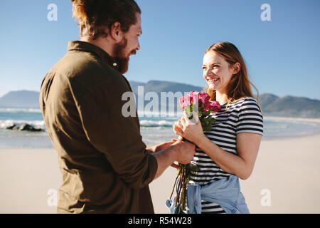 Mann, der überraschung, Blumenstrauß aus Rosen, schöne Frau am Strand. Mann überraschend Freundin auf ein romantisches Date. Verliebtes Paar am Strand. Stockfoto