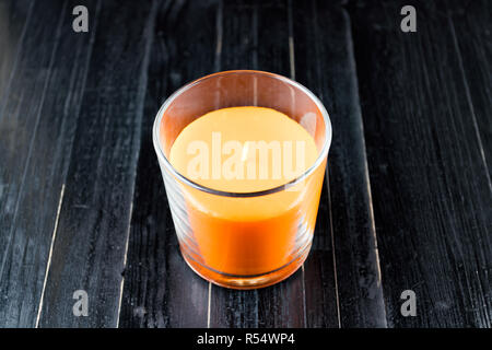 Orange, Kürbis farbige Kerze auf Schwarz natürlichen hölzernen Tisch Hintergrund. Halloween dunkle Stimmung. Stockfoto