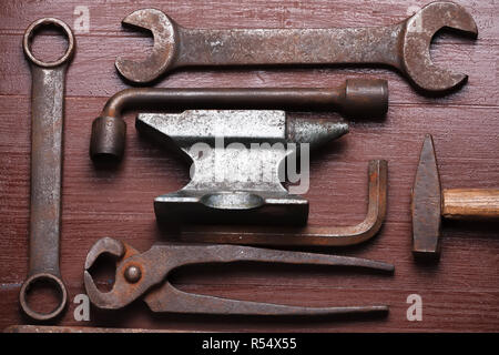 Alten rostigen robuste Amboss und andere Schmied Werkzeuge auf Braun Natur Holz- Hintergrund. Flach Ansicht von oben. Stockfoto