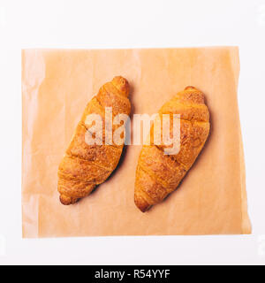 Close-up zwei warme Croissants auf braun Backpapier auf weißem Hintergrund, Ansicht von oben. Stockfoto