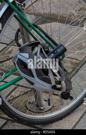 Einen Fahrradhelm auf das Vorderrad eines Fahrrades gesperrt, während durch den Eigentümer links Vorhängeschloss an einen Pfosten. Stockfoto