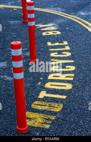 Ein Parkplatz reserviert für Motorräder mit gelben Fahrbahnmarkierungen und orangen und weißen Marker Poller. Stockfoto