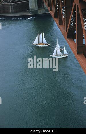 Blick Richtung Süden von hölzernen Segelboote Kreuzfahrt unter der Golden Gate Bridge nach Osten in die San Francisco Bay, während der Pazifik zwischen Yacht Association (PICYA) öffnung Tag Parade, in San Francisco, Kalifornien, 1955. Teil der äußeren Befestigungsmauer von Fort Point (Castille de San Joaquin) ist an der oberen Kante im Hintergrund sichtbar. () Stockfoto