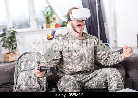 Aufgeregt Soldat in virtual reality Headset spielen Video Game auf der Couch Stockfoto