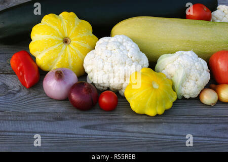 Still-Leben von Gemüse der Saison auf einem rustikalen Holztisch. Grüne Zucchini, gelben Kürbis, Tomaten, Blumenkohl, Paprika und Zwiebeln. Stockfoto