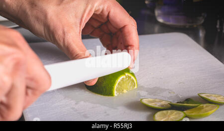 Barkeeper Schnitte grüne Zitronen mit Keramik Messer Stockfoto