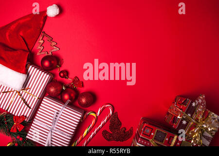 Weihnachten und Neujahr roten Hintergrund dekorierte Geschenkboxen, Santa hat und Spielzeug. Raum Stockfoto