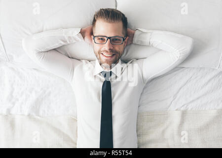 Ansicht von oben. Gut aussehender Geschäftsmann mit Brille liegend auf Bett Stockfoto