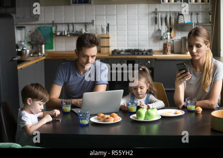 Eltern mit Laptops und Smartphones frühstücken mit Kind Stockfoto