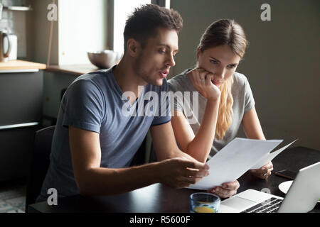 Ernsthafte junge Paar prüfen Dokumente mit Laptop Stockfoto