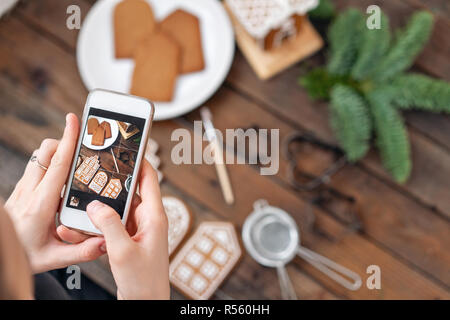Das Mädchen macht ein Foto Flatley für soziale Netzwerke, das Ergebnis ihrer Arbeit. Bloggen, Blogger. Viel Ingwer Kekse. Weihnachtliche Stimmung, winter Morgen. Tannenzweigen und Formen zum Backen. Stockfoto