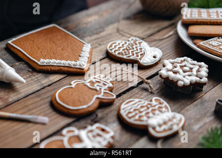 Viel Ingwer Kekse in unterschiedlicher Form auf braune Holztisch. Mit weißen süßen Glasur dekoriert. Weihnachtliche Stimmung, winter Morgen. Tannenzweigen Stockfoto