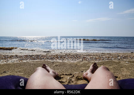 Die Beine eines Mannes auf einem Strand Hintergrund. Ein Mann liegt auf einer Amatrace am Strand und ruht. Beine in den Rahmen. Stockfoto