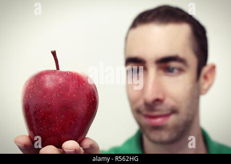 Mann lächelnd und suchen bei Red Apple, der auf seiner rechten Hand isoliert auf weißem Stockfoto