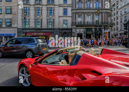 London, Großbritannien - 22 April, 2018: Paar in einem oben offenen roten Ferarri Auto auf der Straße in der Nähe des Trafalgar Square. Pflaster hat sich Massen von Menschen zu Fuß. Stockfoto